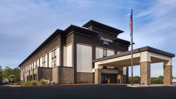 A Hampton Inn hotel with a modern design, featuring a clear entrance, a welcoming sign, and a flagpole.