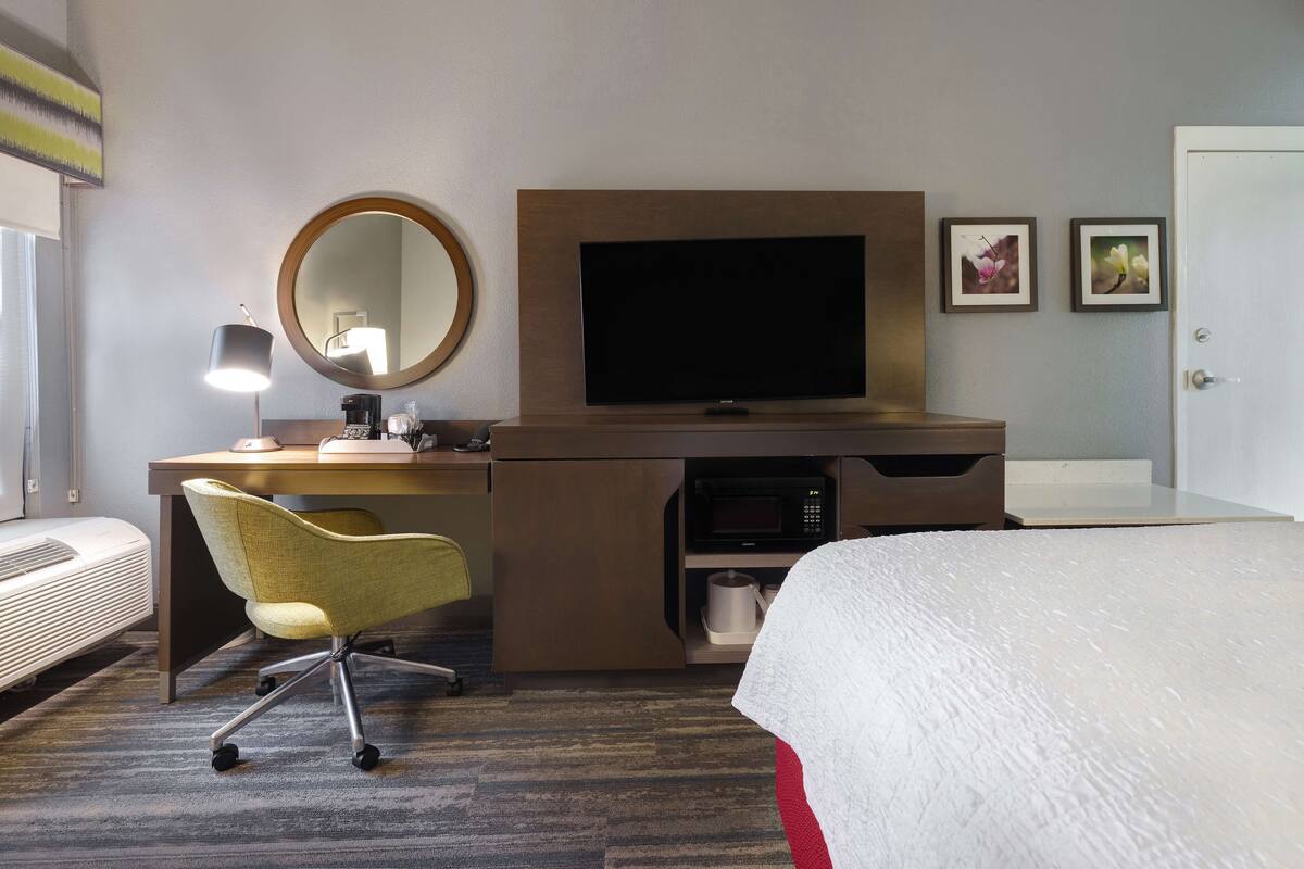 A hotel room with a bed, a desk with a computer, a chair, a television, and a microwave.