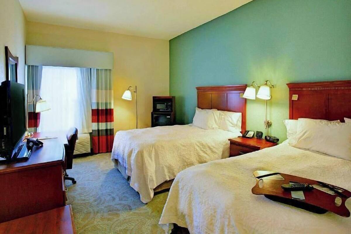 A hotel room with two beds, a desk with a telephone, a television, and a bedside table with lamps.