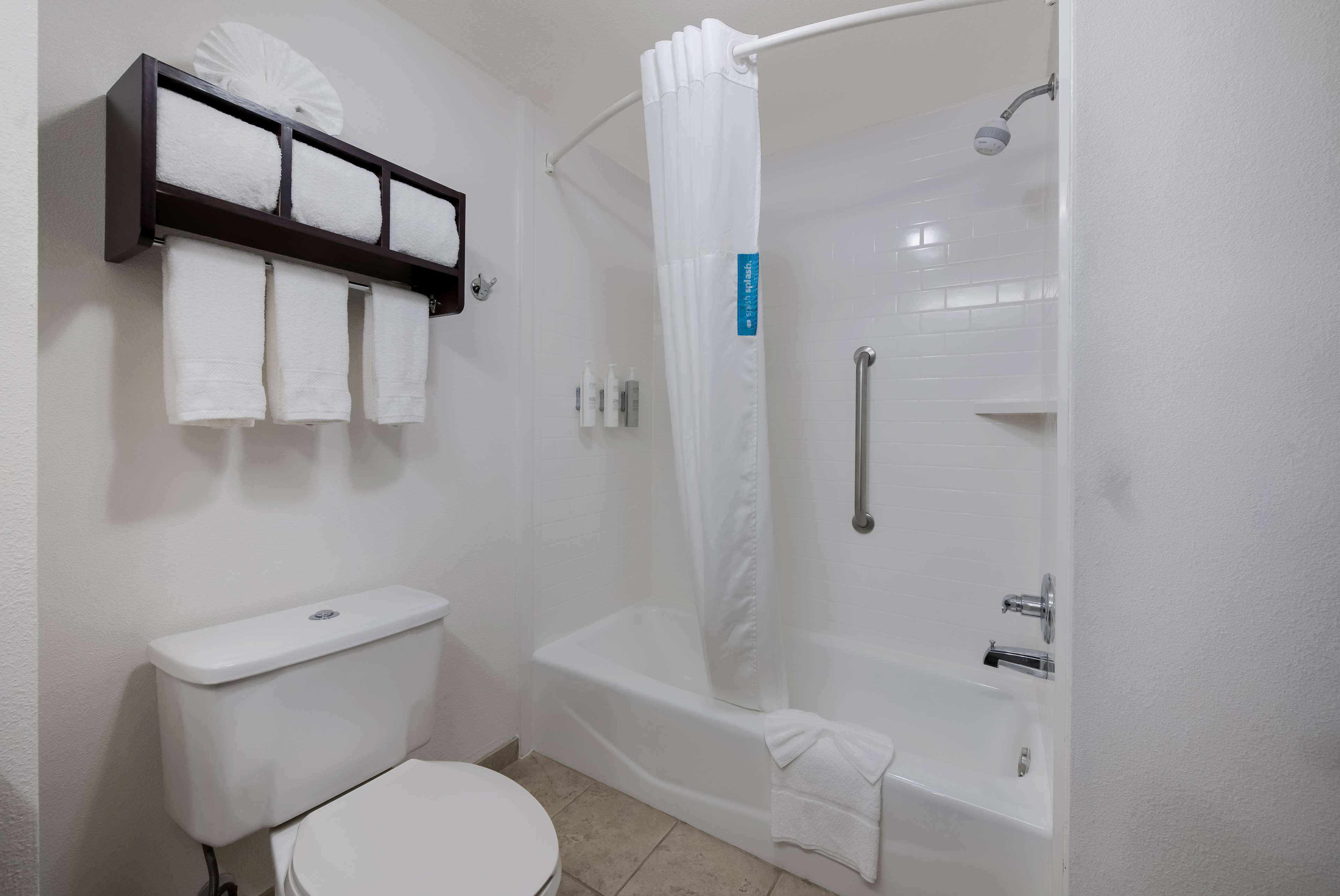 A bathroom with a toilet, a bathtub, and a shower curtain. There are towels hanging on a rack above the toilet.