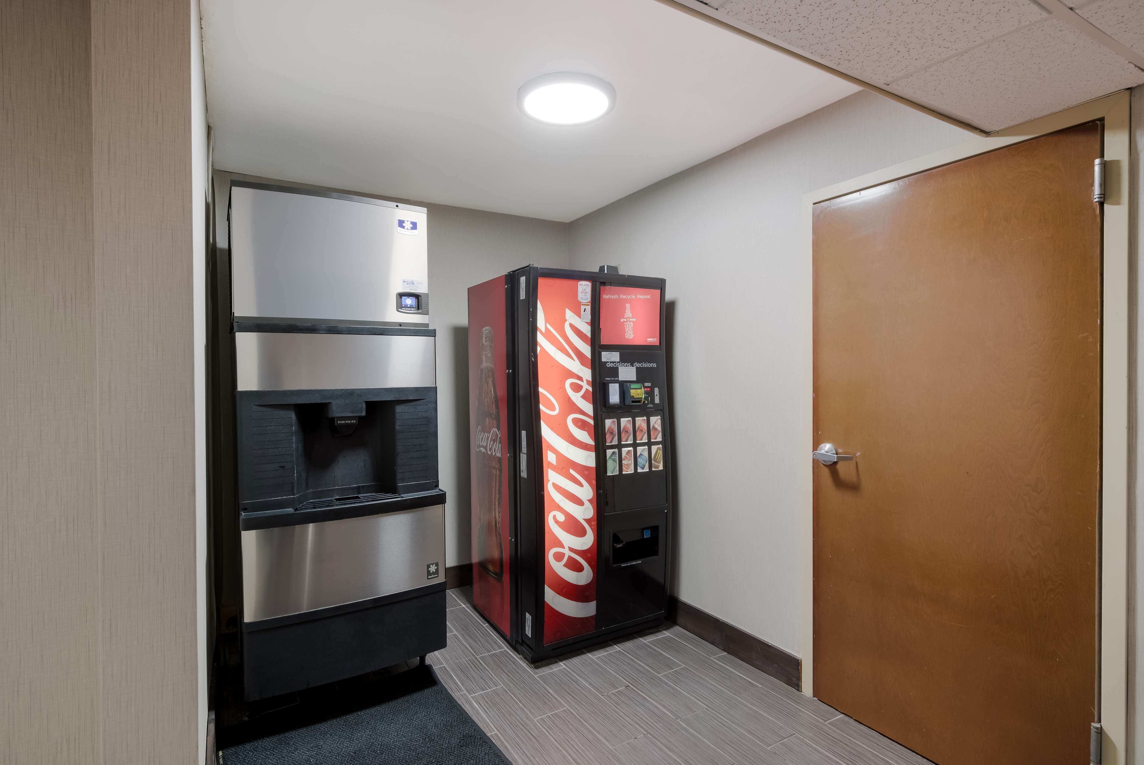 A hallway with a Coca-Cola refrigerator, a water dispenser, and a door.