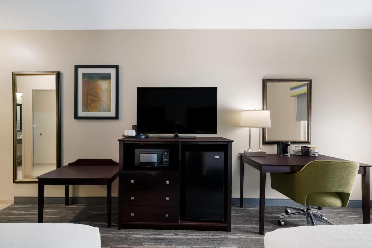 Habitación de hotel con cama, escritorio con televisor, microondas, refrigerador, silla y espejo.