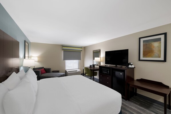 A hotel room with a large bed, a desk with a computer, a television, and a window with blinds.