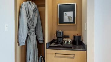 A hotel room with a robe hanging, a coffee maker, a framed picture, and a small ironing board.