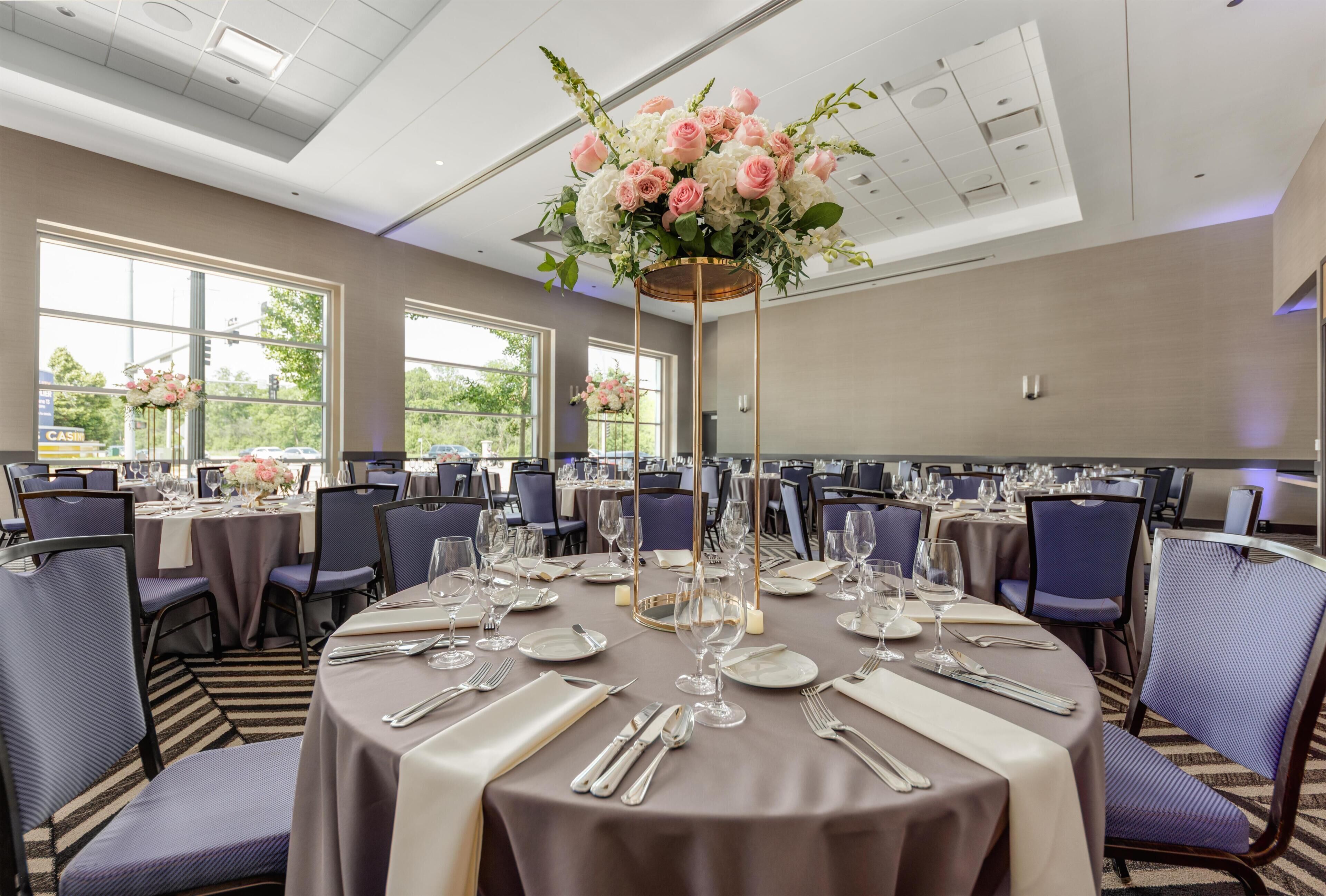 A banquet hall with round tables, chairs, and floral centerpieces.