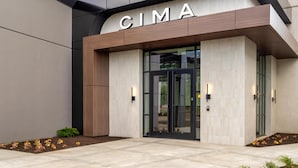 A modern building entrance with a 'CIMA' sign, glass doors, and a tiled pathway. - Hyatt Centric Chicago O'Hare (Rosemont)