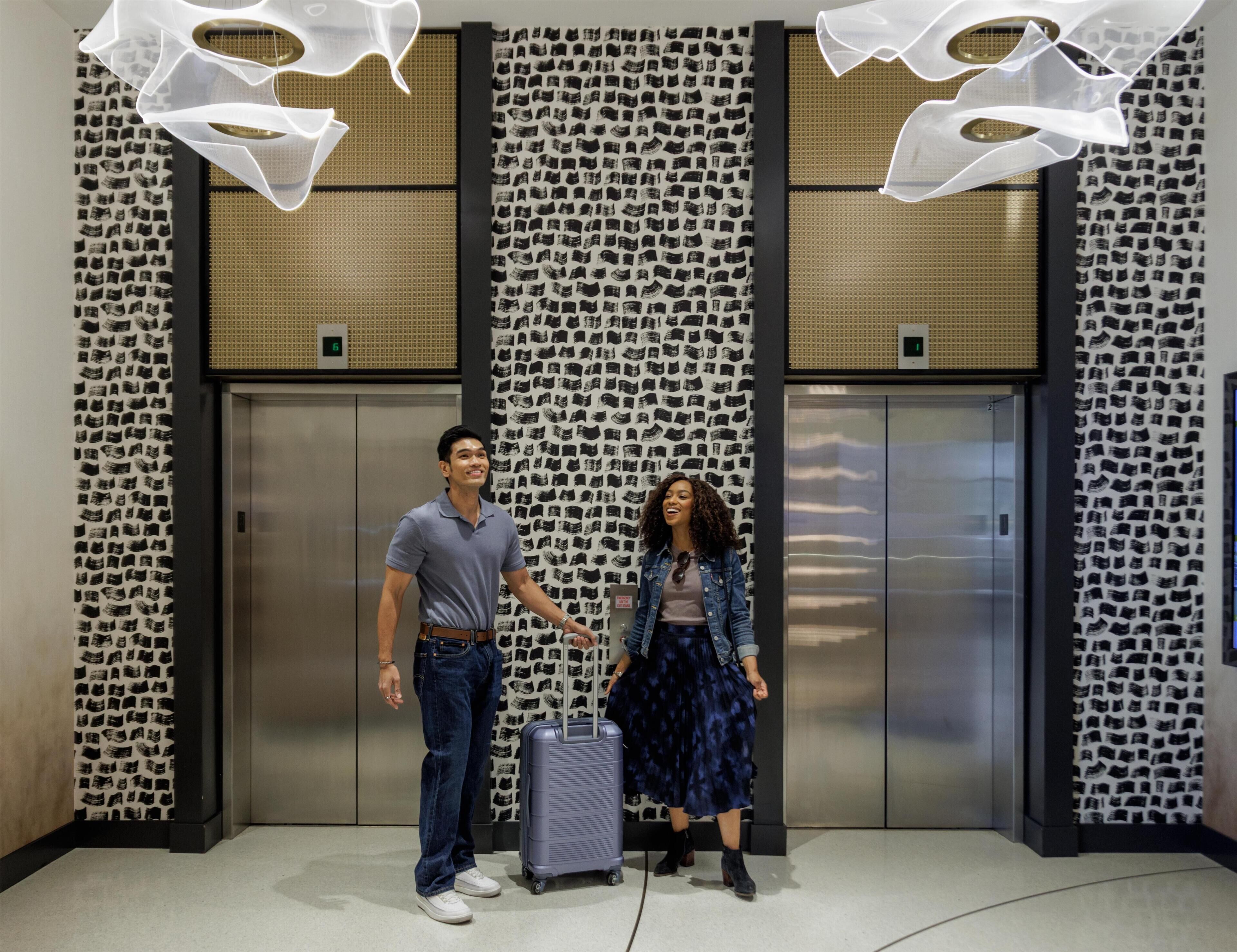 A man and a woman standing in front of elevators with patterned walls and a modern design.