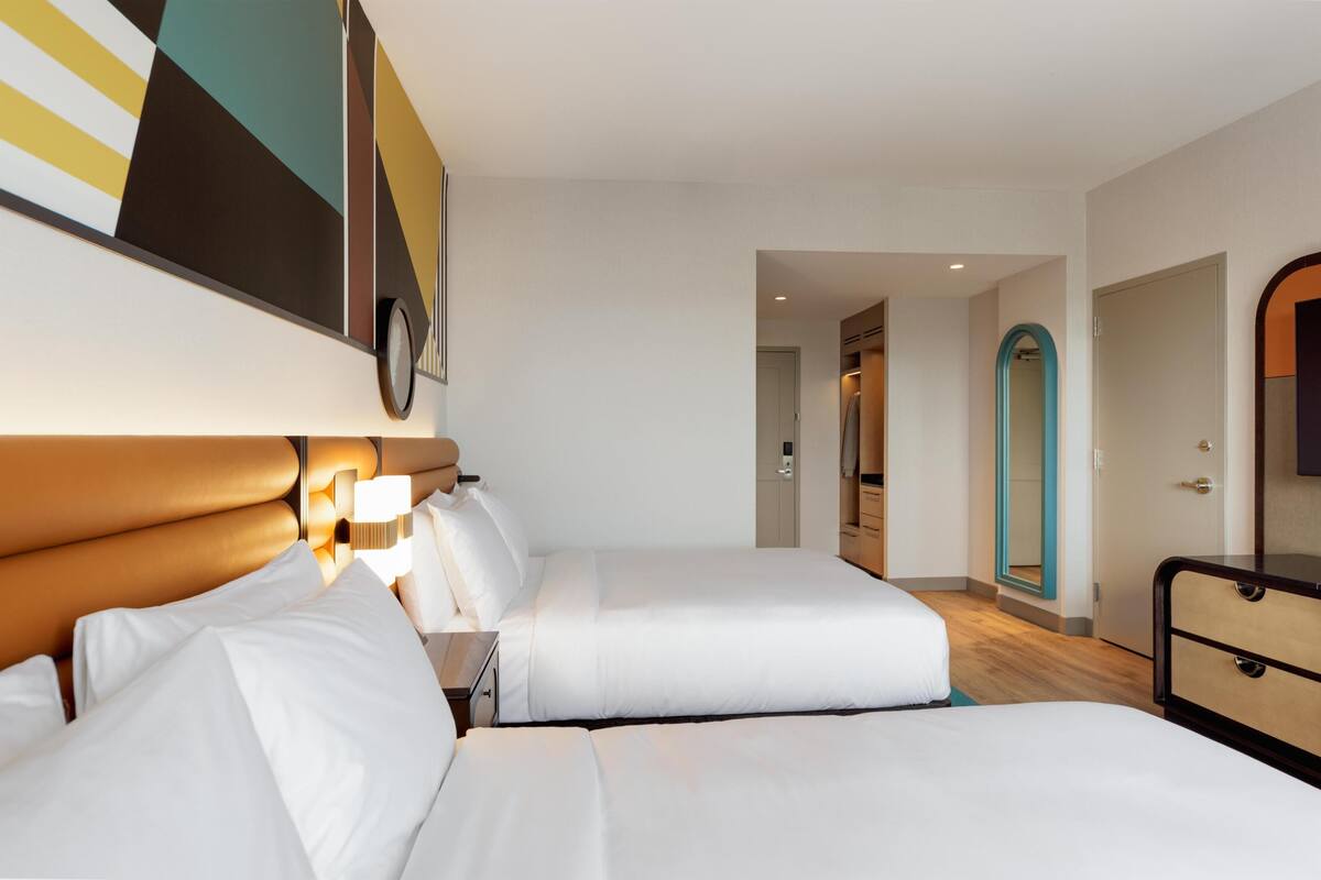 A hotel room with two beds, a large mirror, and a view of the hallway.