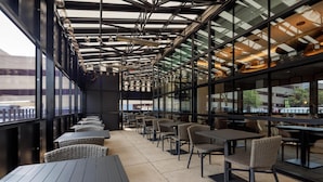 An outdoor cafe area with tables and chairs, large windows, and a modern ceiling design. - Hyatt Centric Chicago O'Hare (Rosemont)