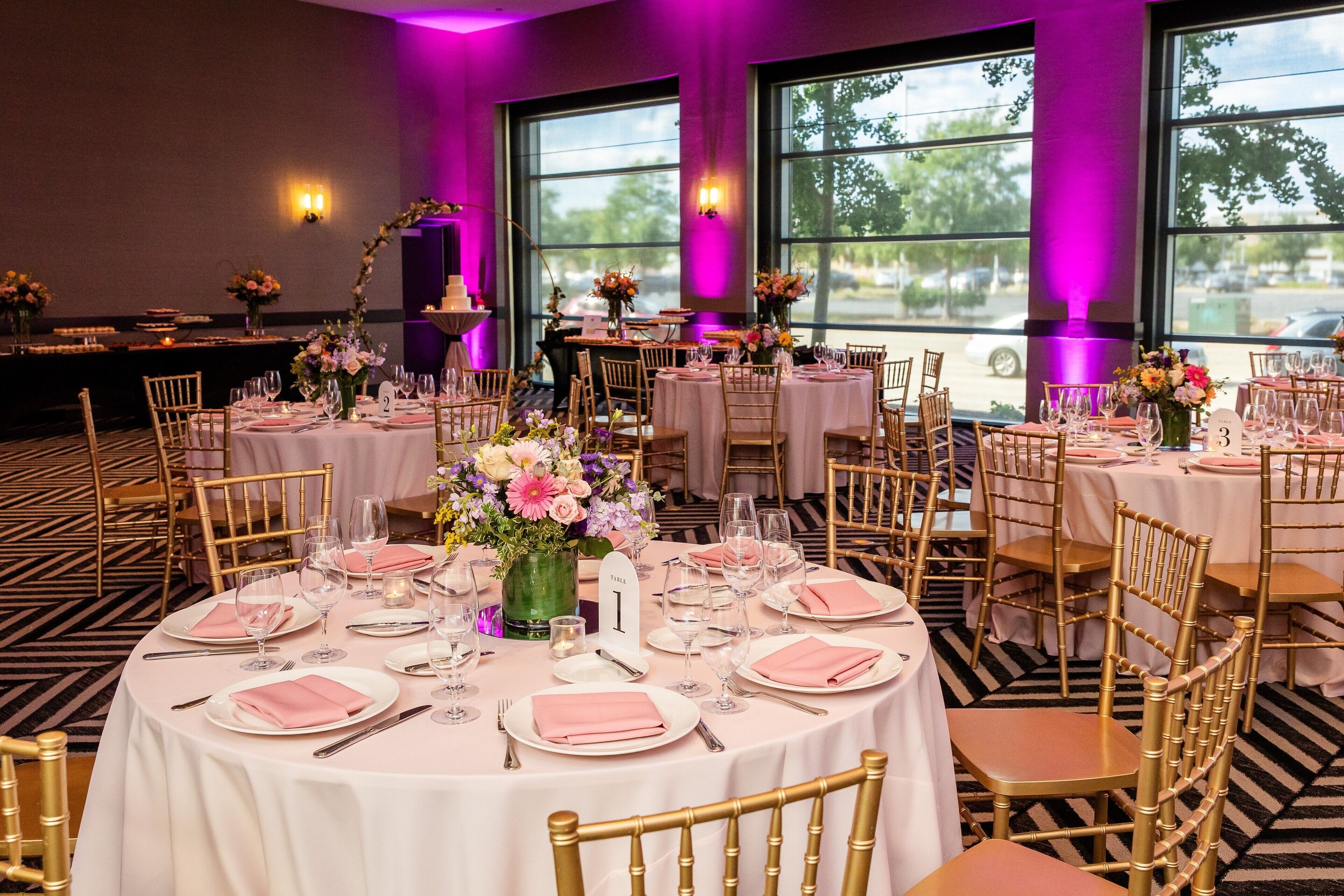 Een feestzaal met ronde tafels, ingericht voor een formeel evenement, met gouden stoelen en witte tafelkleden.