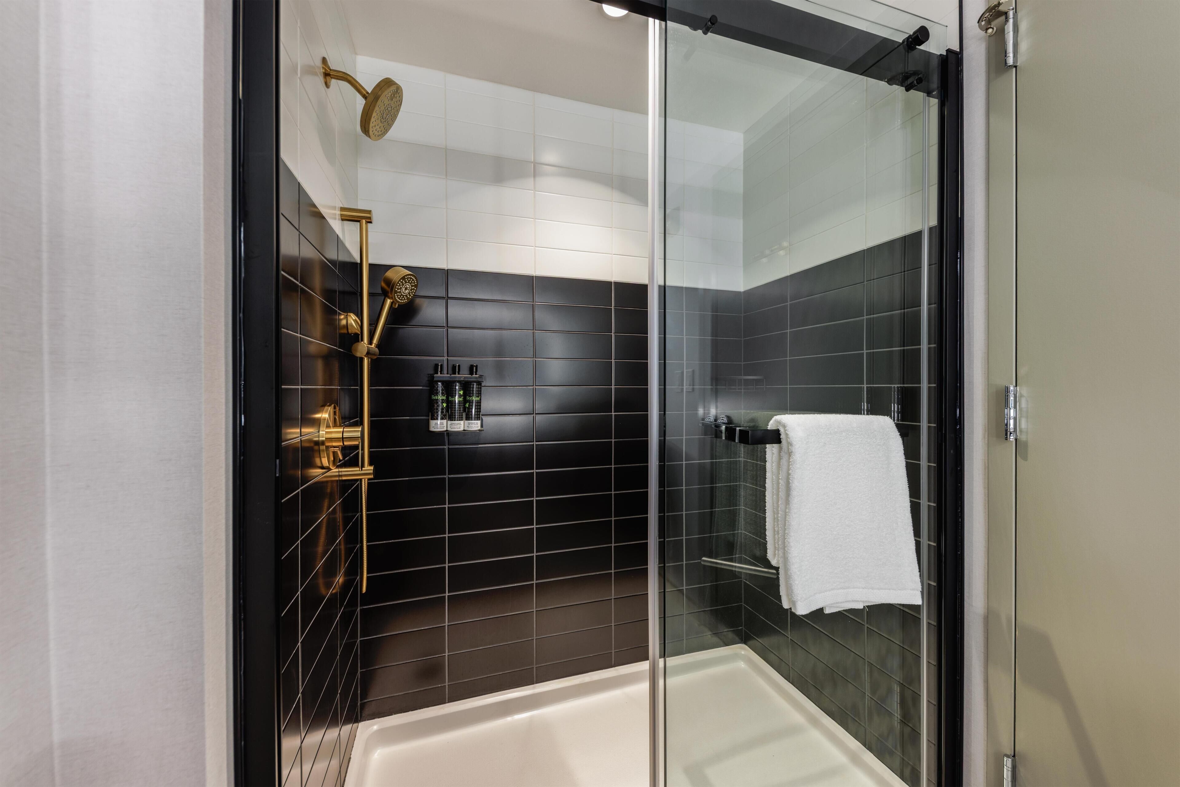 Une salle de bain moderne avec une douche à l’italienne en verre, des carreaux noirs et une baignoire blanche.