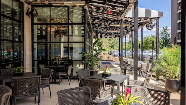 An outdoor patio area with wicker furniture, potted plants, and a covered seating area with a view of the street. - Hyatt Centric Chicago O'Hare (Rosemont)
