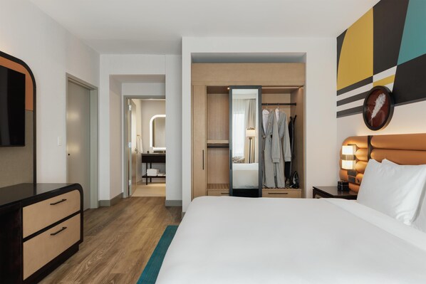 Una habitación de hotel con una cama, un armario, un espejo y una mesita de noche.
