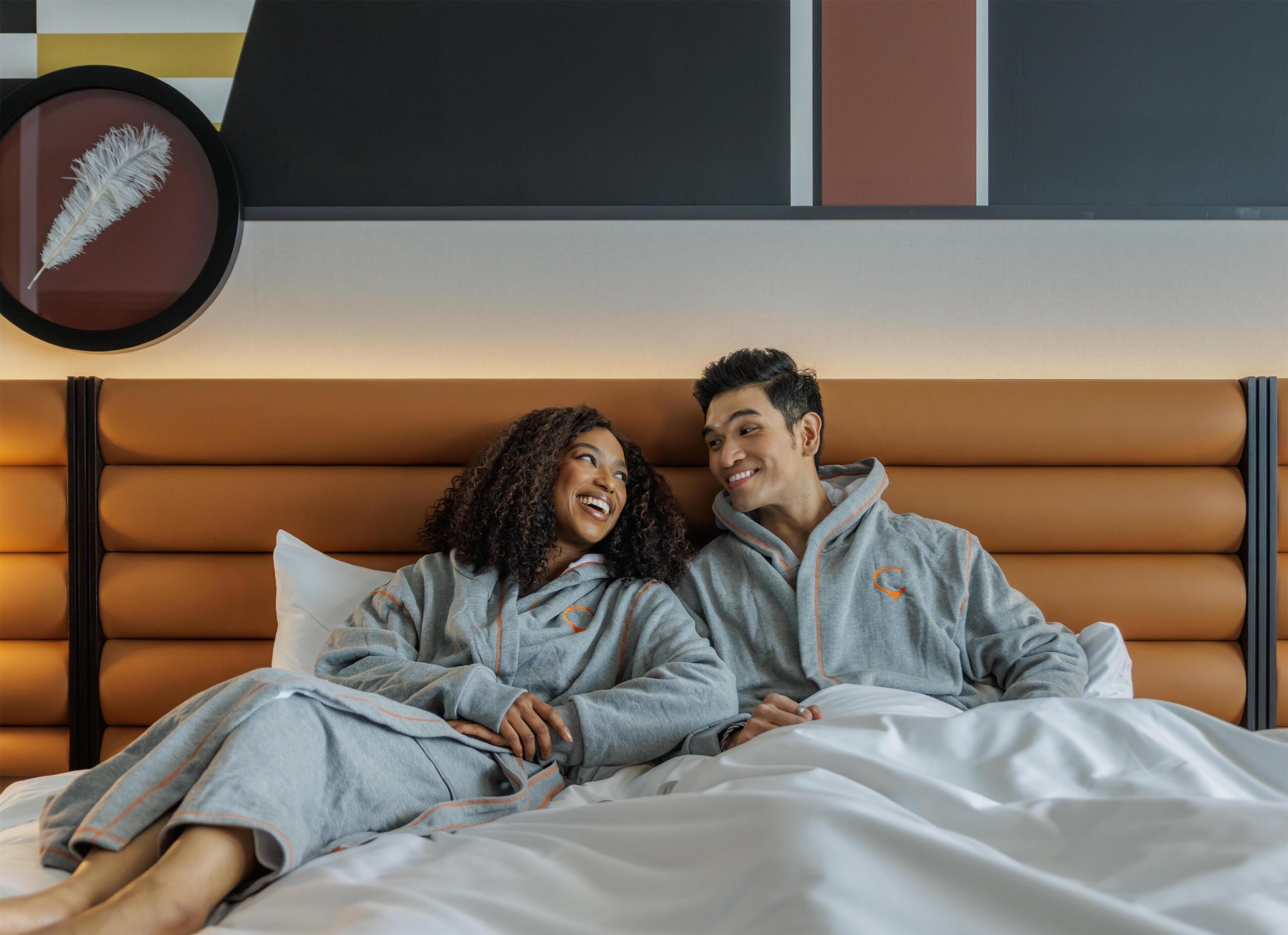 Una cama con cabecera marrón, un adorno de plumas y una pared con patrones geométricos.