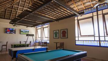 A pool table with a blue felt surface, a ceiling fan, and a thatched roof structure.