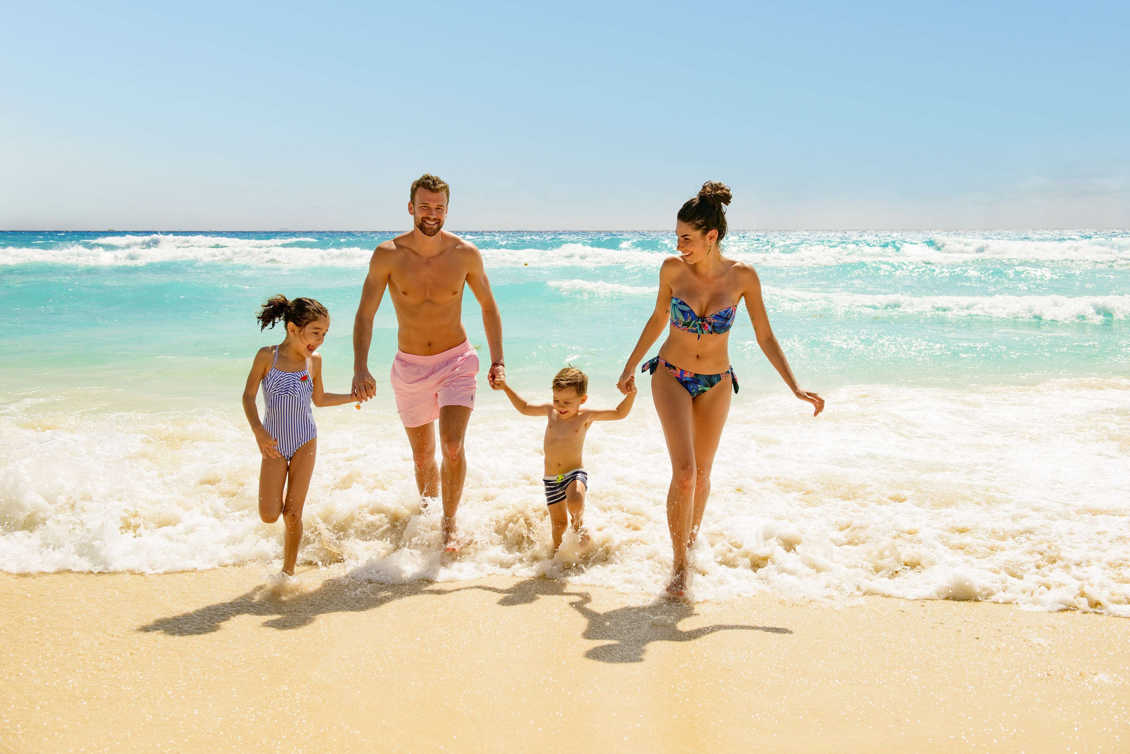 A family walking on a sandy beach with waves in the background.