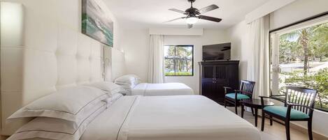 A hotel room with two beds, a ceiling fan, a TV, and a balcony with chairs.