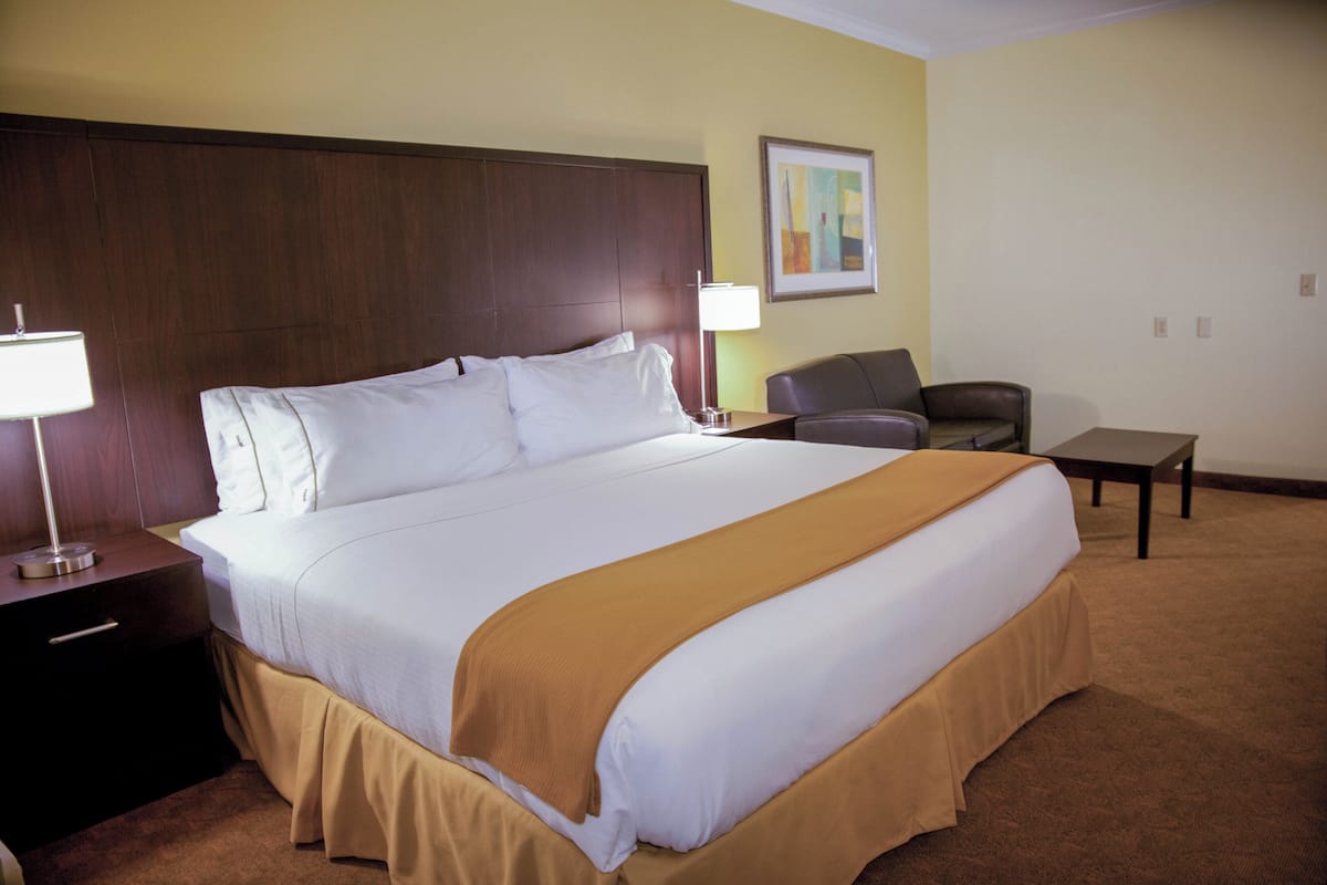 A hotel room with a large bed, a nightstand with a lamp, a chair, and a small table.