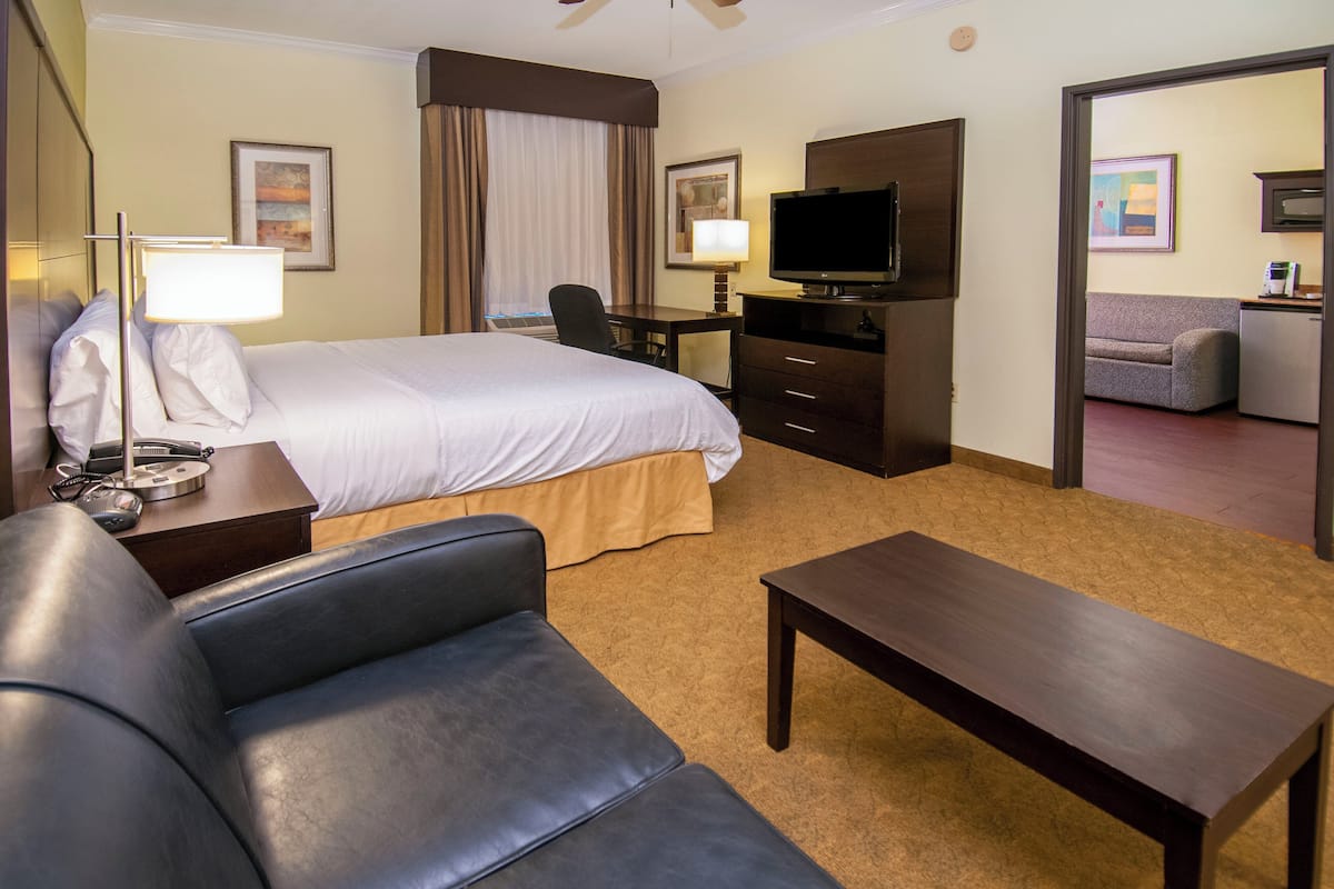 A hotel room with a large bed, a desk with a chair, a television, and a sofa.
