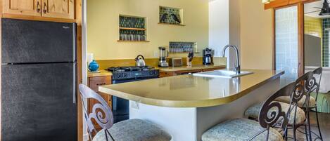 Una cocina con un refrigerador negro, armarios de madera, una isla grande con taburetes de bar y un microondas.