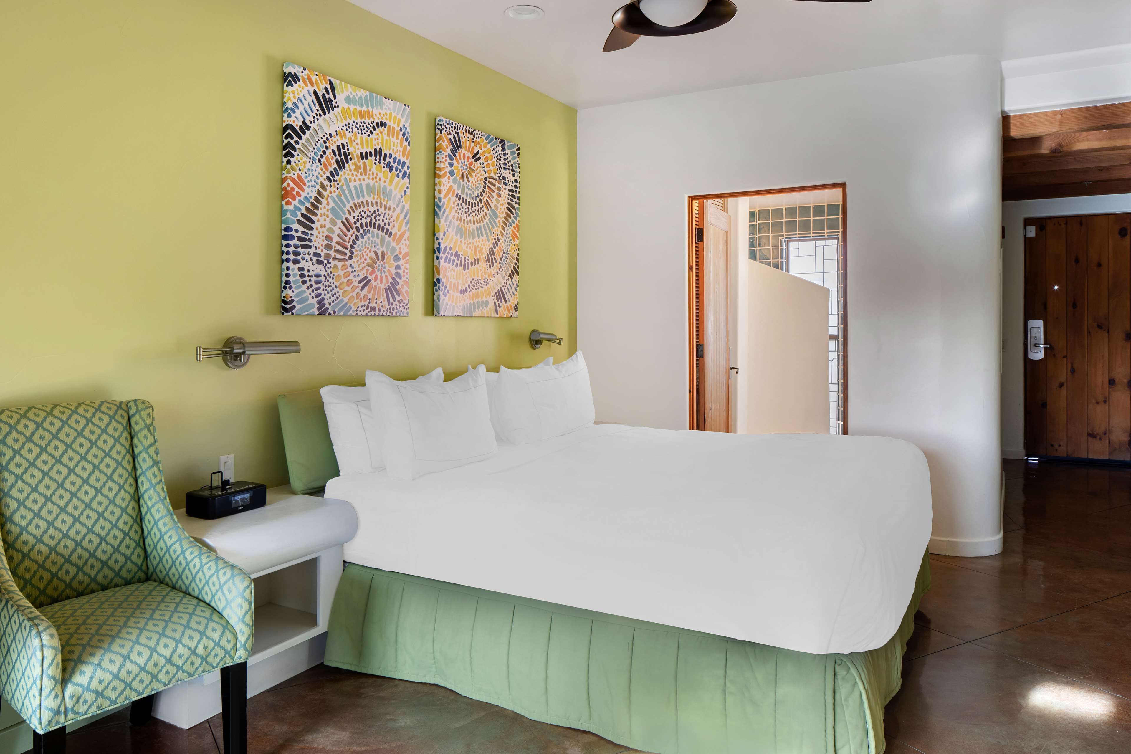 Una camera da letto con un letto grande, una poltrona verde e due dipinti astratti alle pareti.