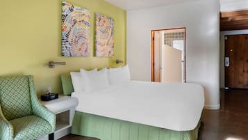 Una camera da letto con un letto grande, una poltrona verde e due dipinti astratti alle pareti.