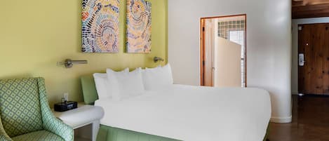 A bedroom with a large bed, a green armchair, and two abstract paintings on the wall.