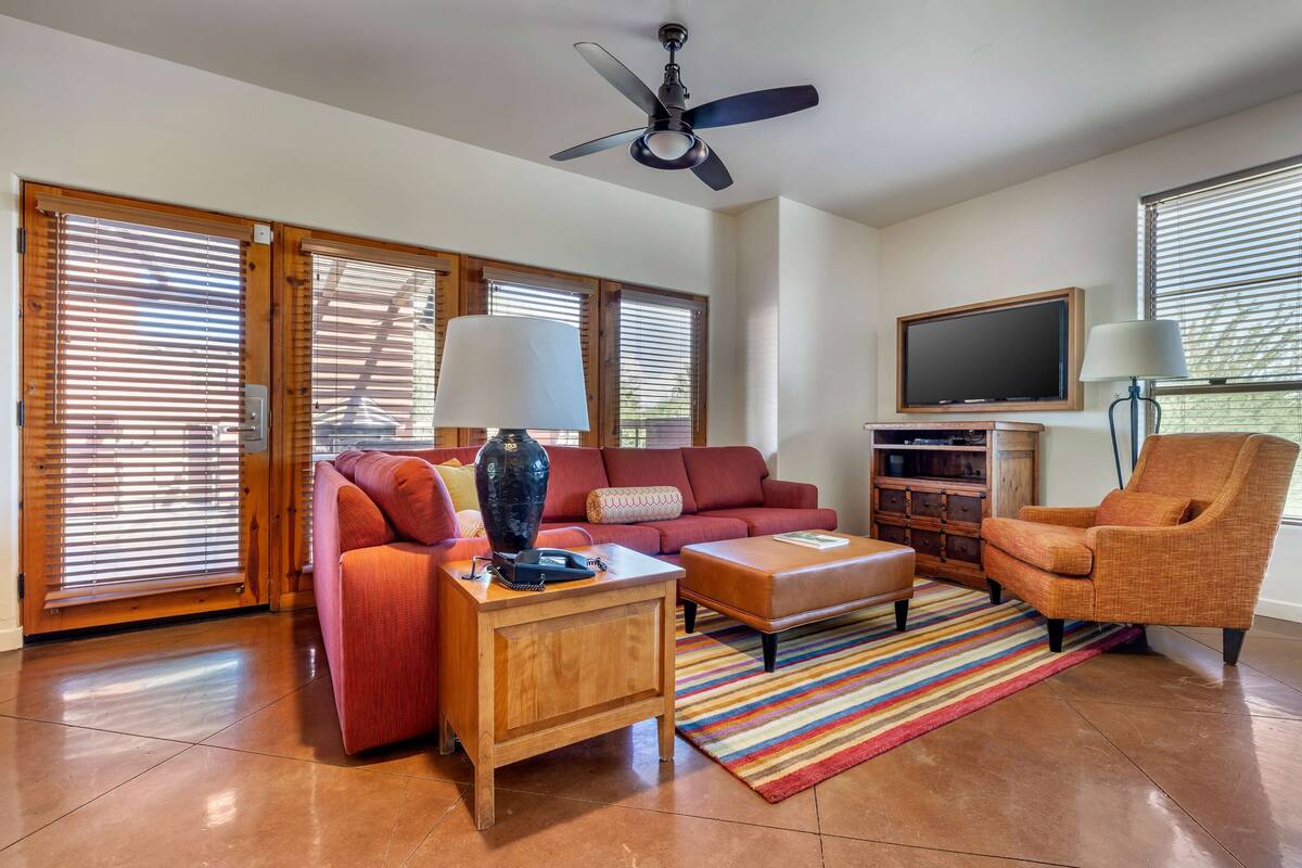 A living room with a red sofa, a wooden side table, a striped rug, a television, and a ceiling fan.