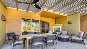 Une terrasse extérieure avec une table en bois et des chaises en osier, un ventilateur de plafond et une vue sur l’extérieur.