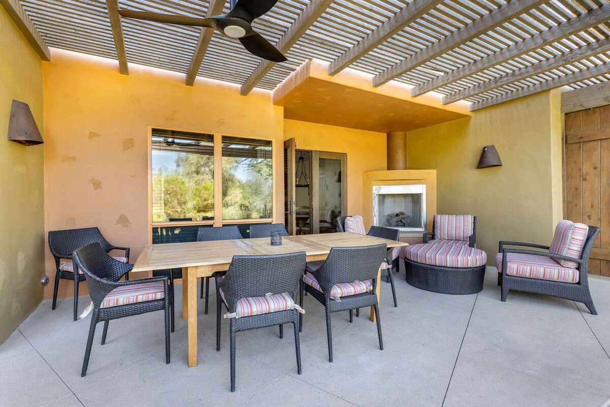 An outdoor patio with a wooden table and wicker chairs, a ceiling fan, and a view of the outdoors.