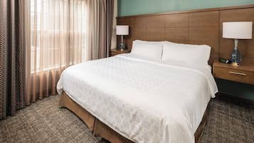 A hotel room with a large bed, two bedside tables with lamps, a wooden headboard, and a view of the outdoors through sheer curtains.