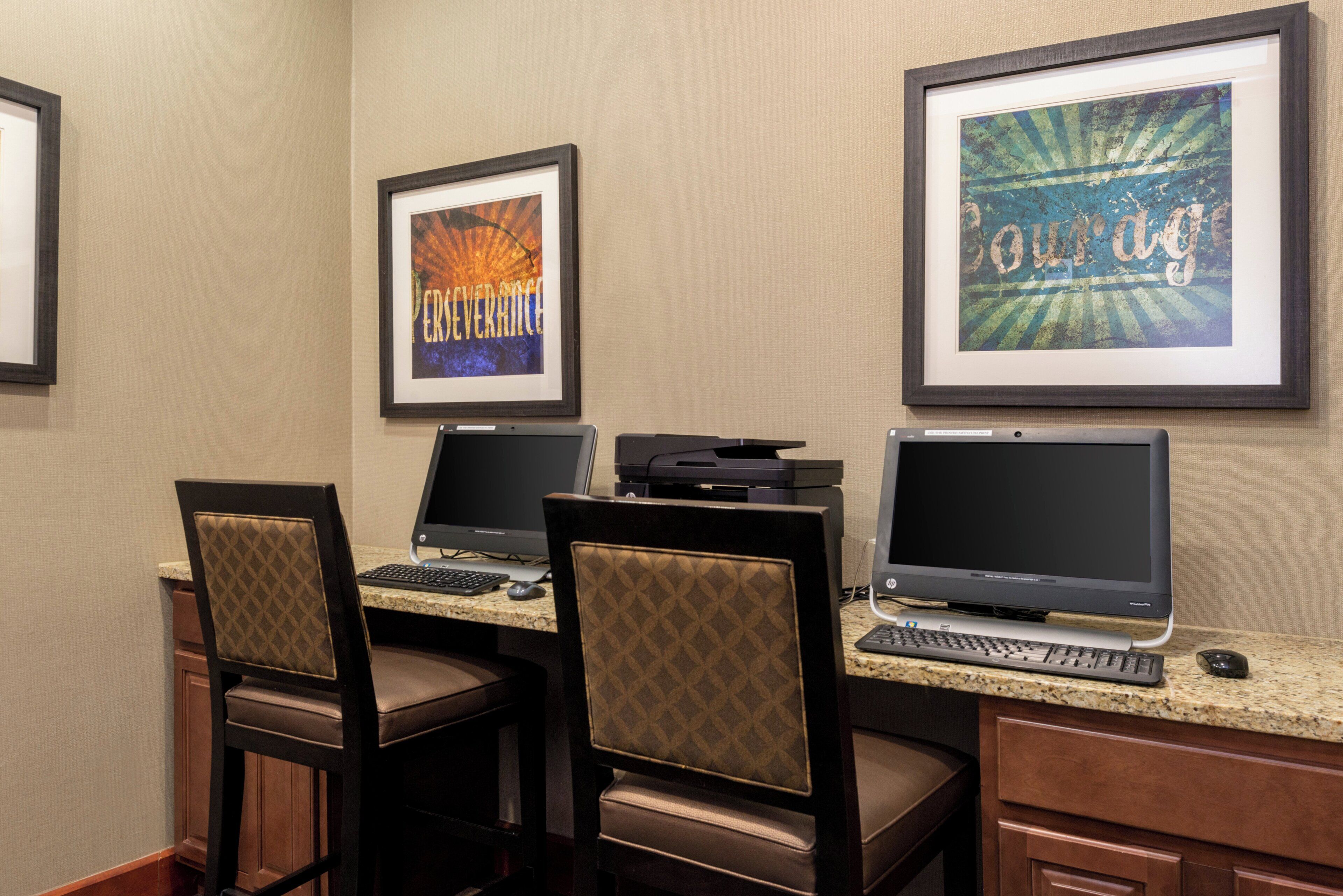 A hotel room with three workstations, each with a computer and keyboard, and a framed picture on the wall.