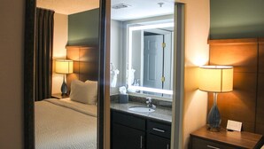 Ein Hotelzimmer mit einem Bett, einem Badezimmer mit Waschbecken und Spiegel sowie einem Nachttisch mit Lampe.