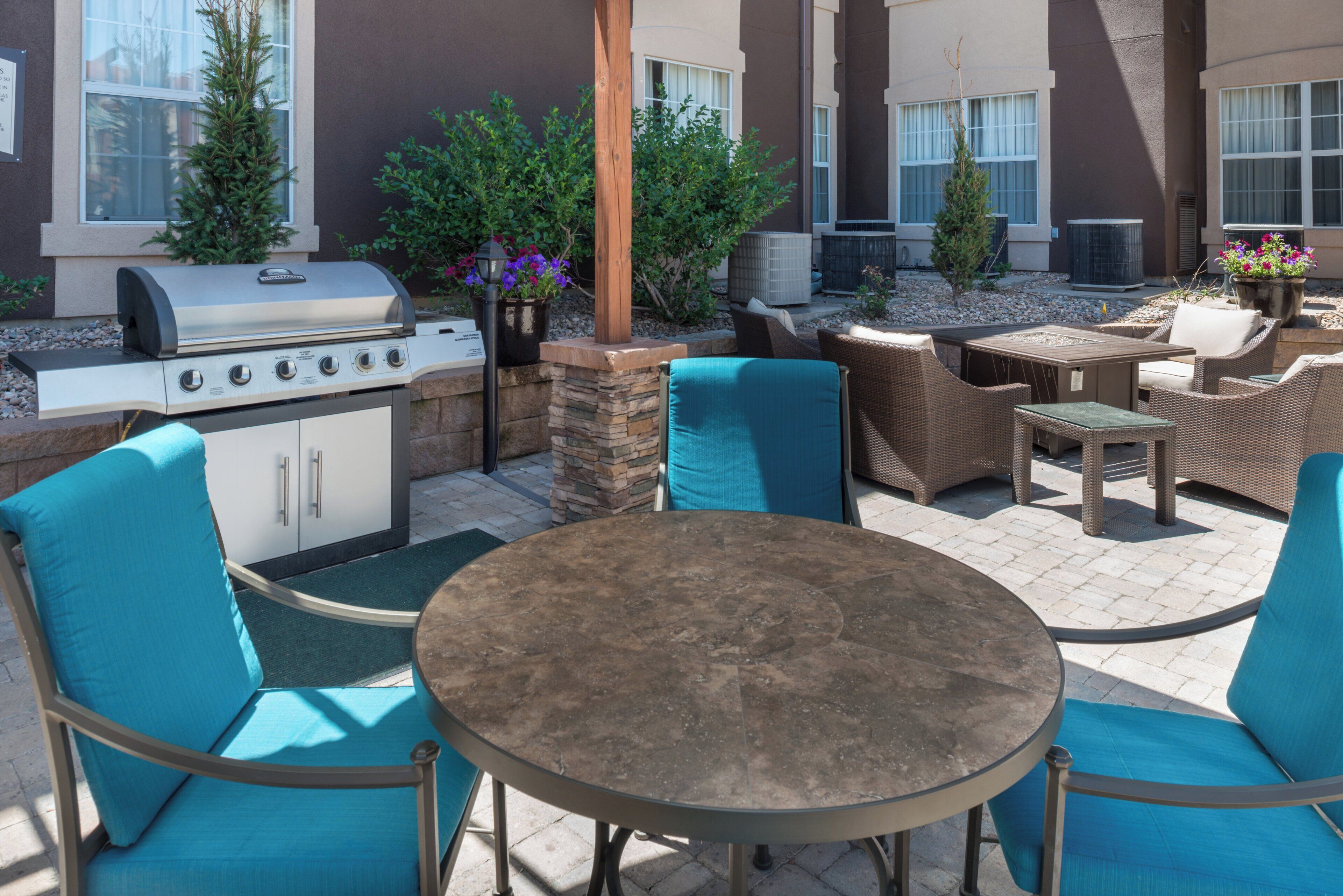 Eine Terrassensitzgelegenheit draußen mit Grill, Möbeln und Pflanzen in Töpfen.
