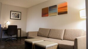 Ein Hotelzimmer mit Sofa, Schreibtisch mit Stuhl und Lampe. An der Wand hängen drei Bilder.