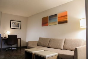 Camera d'albergo con divano, una scrivania con sedia e una lampada. Tre quadri alle pareti.