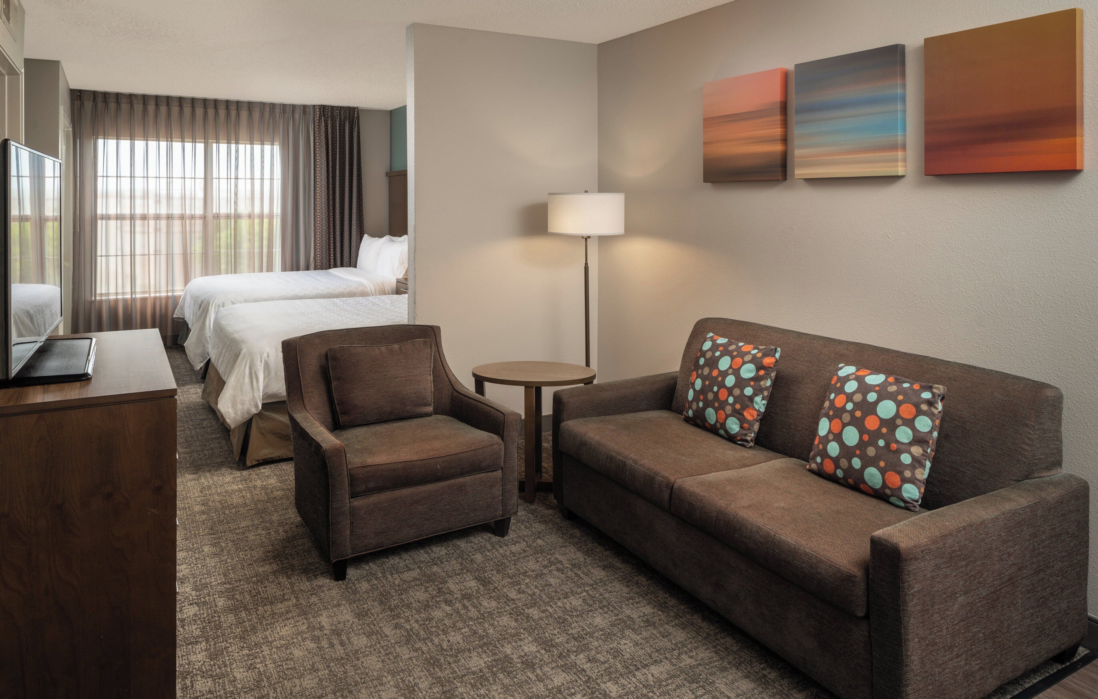 A hotel room with a bed, a sofa, a chair, a desk, and a lamp.