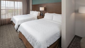 A hotel room with two beds, a nightstand, a lamp, and a view of the outdoors through large windows.