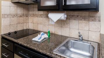 A kitchen with a granite countertop, stainless steel sink, and black cabinets.