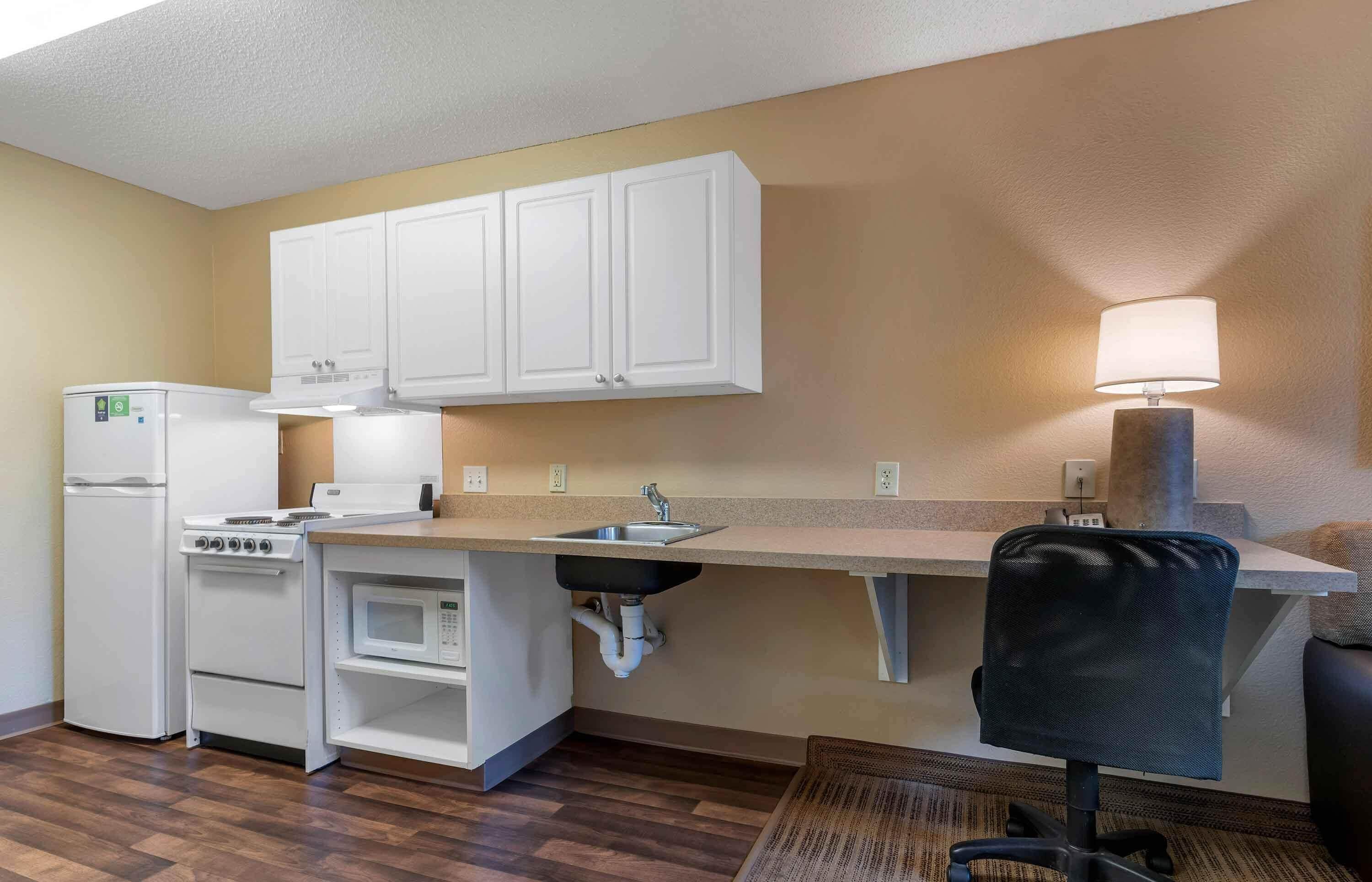 A compact kitchen with white cabinets, a stove, a microwave, and a sink.
