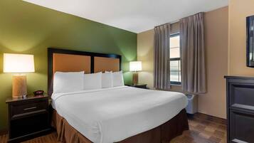 Habitación de hotel con cama, dos mesitas de noche, lámpara, ventana con cortinas y televisor montado en la pared.