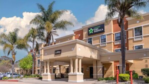 A Stay America hotel with a lobby entrance, palm trees, and a clear sky.