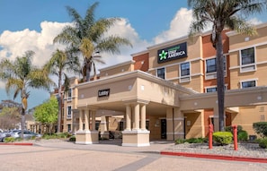 A Stay America hotel with a lobby entrance, palm trees, and a clear sky.