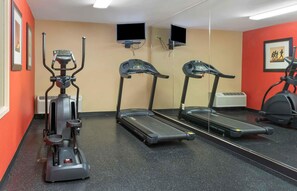Une salle de sport équipée de matériel d’exercice, notamment un vélo d’appartement, deux tapis de course et un mur avec des miroirs.