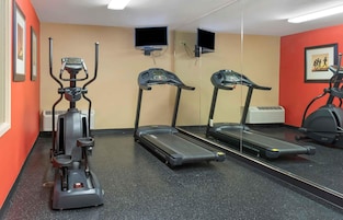 A gym with exercise equipment including a stationary bike, two treadmills, and a mirrored wall.