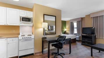 Habitación de hotel compacta con kitchenette, cama, escritorio, silla, televisión y ventana con cortinas.