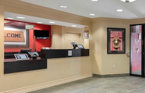 Un espace d’accueil avec une pancarte « BIENVENUE », un comptoir d’accueil, une porte et un écran fixé au mur.
