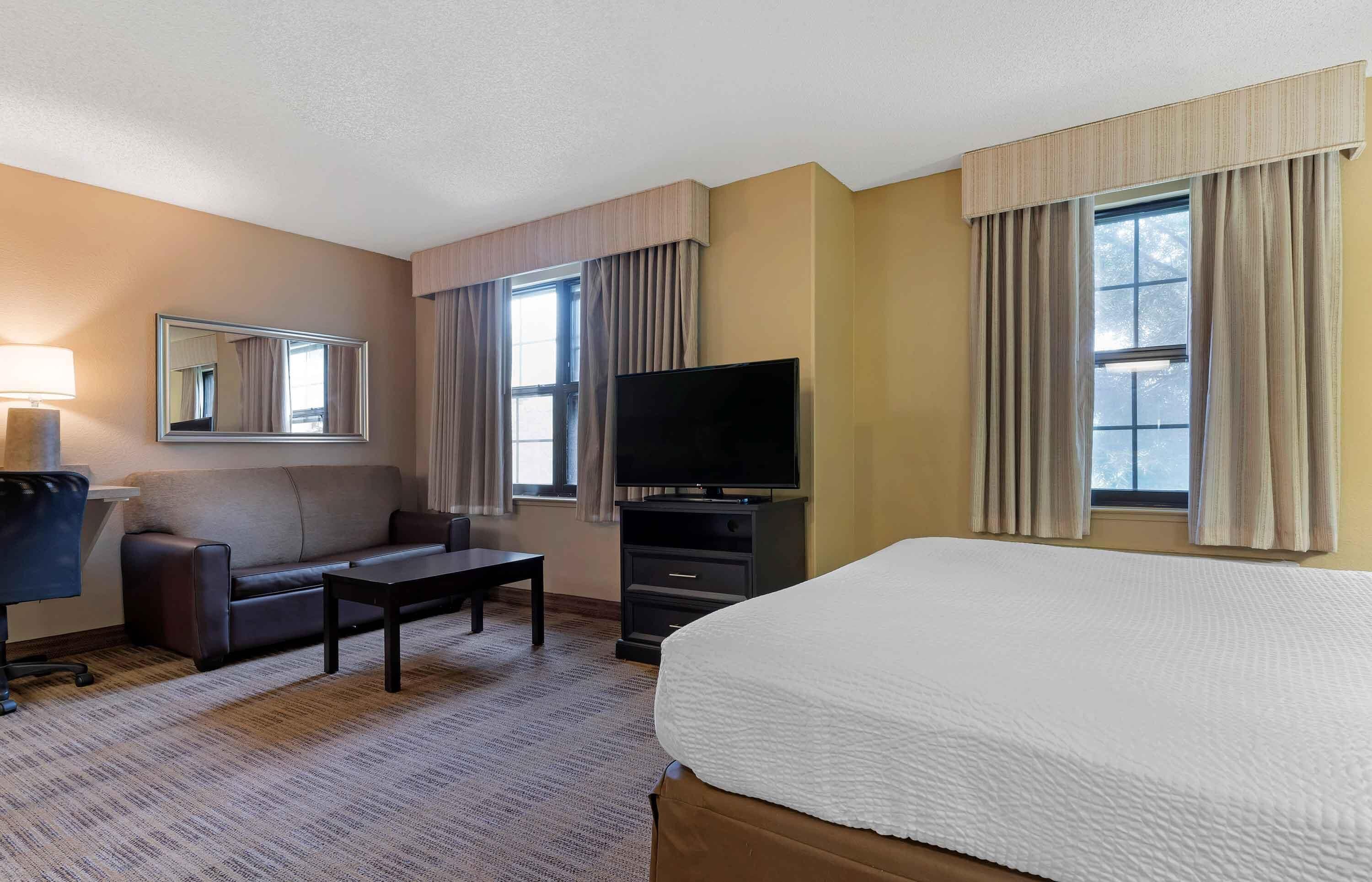 A hotel room with a bed, a sofa, a TV, a desk, and a chair.