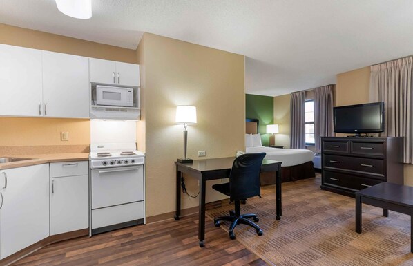 A hotel room with a kitchenette, a bed, a desk, and a TV.