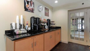 A breakfast bar with coffee makers, cups, and condiments.